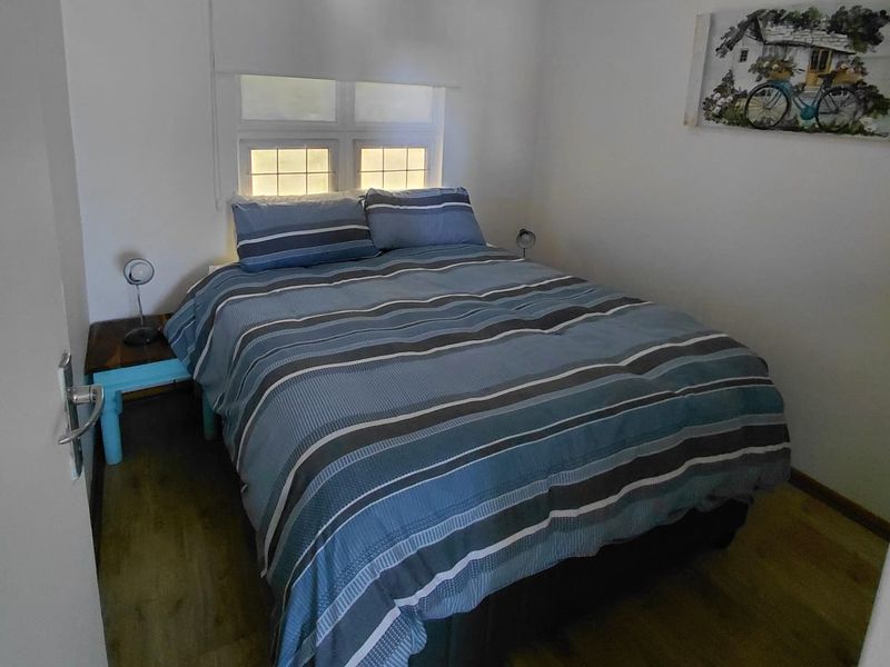 A compact bedroom featuring laminate flooring and a window fitted with a roller blind.