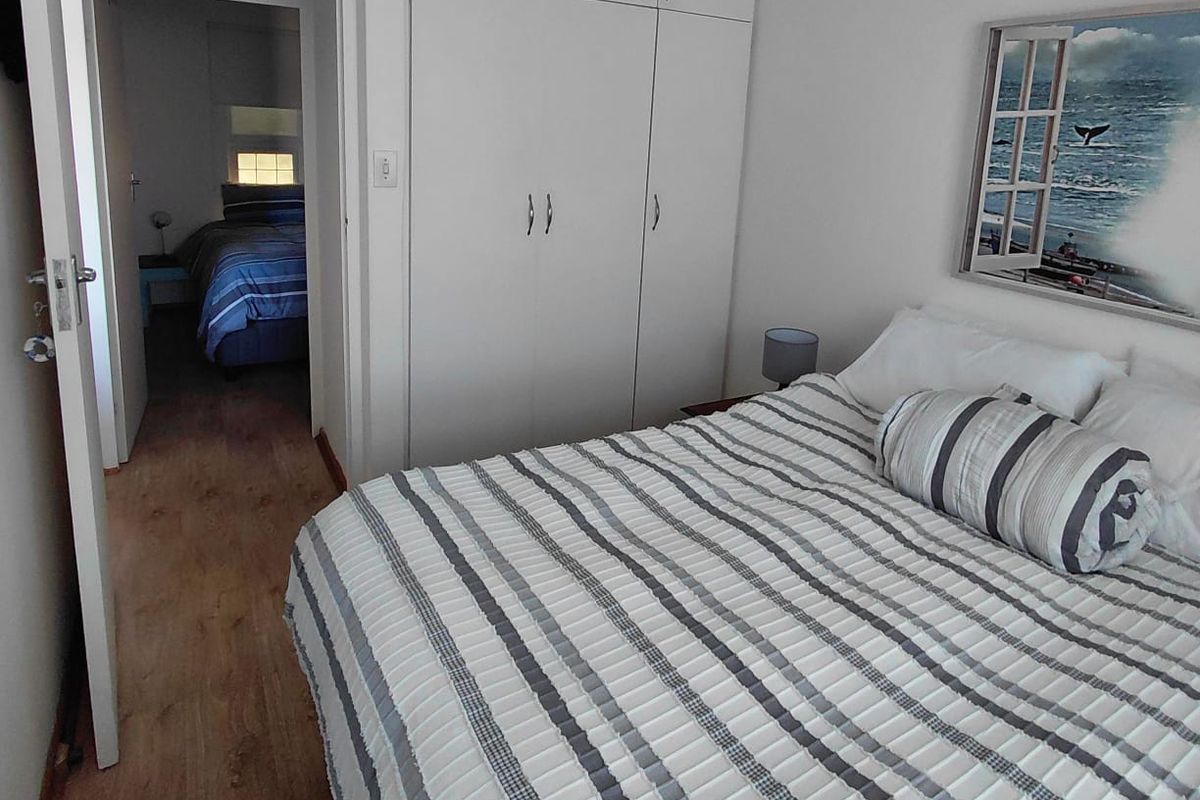 A well-maintained bedroom featuring built-in cupboards, laminate flooring, and a view into an adjacent bedroom.
