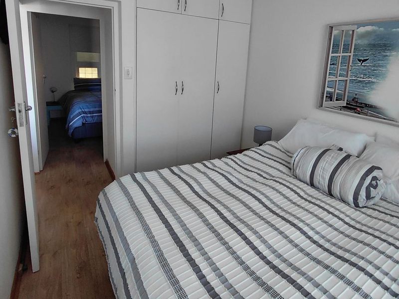 A well-maintained bedroom featuring built-in cupboards, laminate flooring, and a view into an adjacent bedroom.