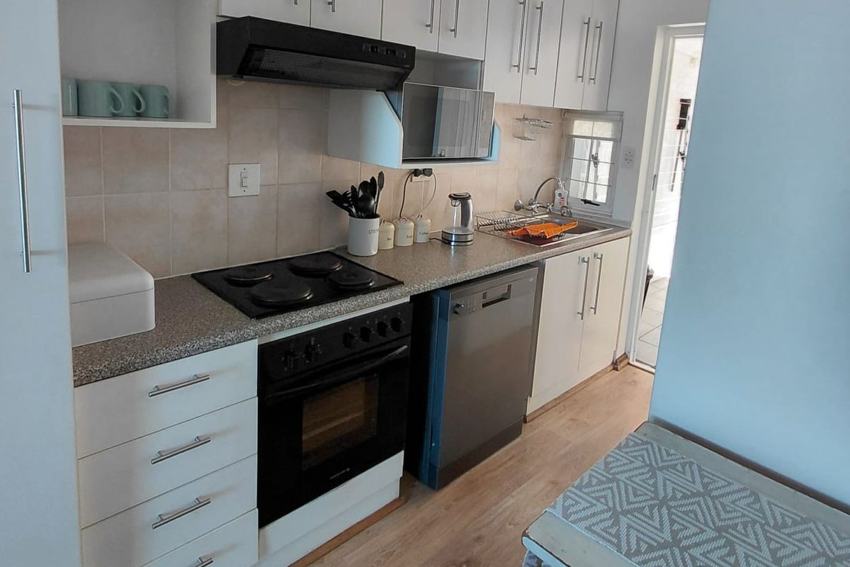 A functional galley-style kitchen featuring white cabinetry, laminate countertops, integrated oven and hob, and light wood-look flooring.