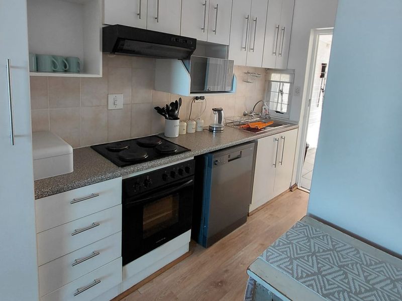A functional galley-style kitchen featuring white cabinetry, laminate countertops, integrated oven and hob, and light wood-look flooring.