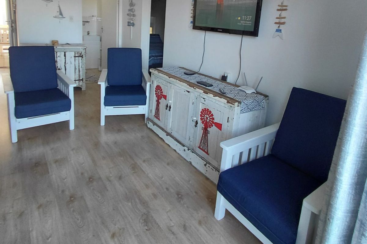 A living room area featuring light-toned laminate flooring and a wall-mounted television, with access to adjacent rooms visible in the background.