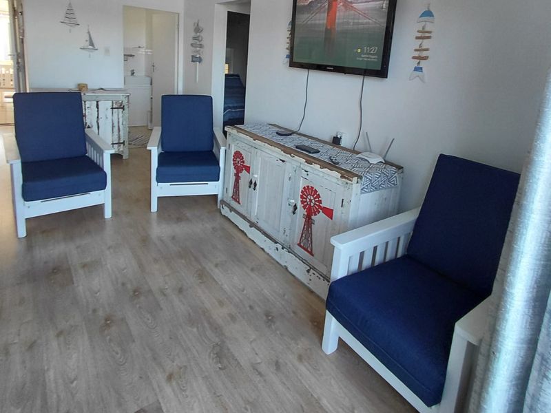 A living room area featuring light-toned laminate flooring and a wall-mounted television, with access to adjacent rooms visible in the background.