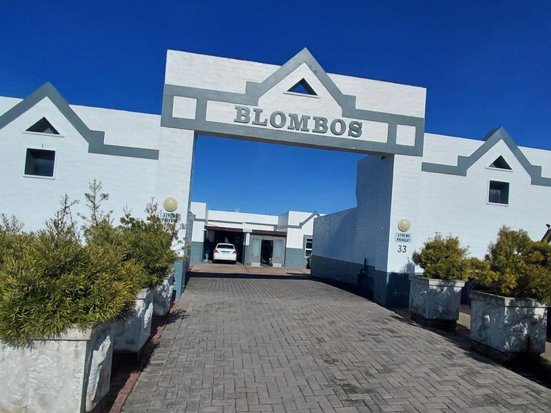 Front entrance view of the Blombos apartment complex featuring a paved driveway and a prominent architectural archway.