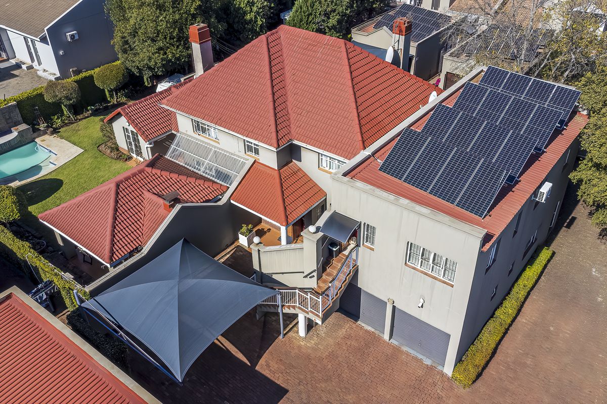 Aerial view of a residential property featuring a tiled roof, integrated solar panels, a swimming pool, and a paved driveway with a double garage.