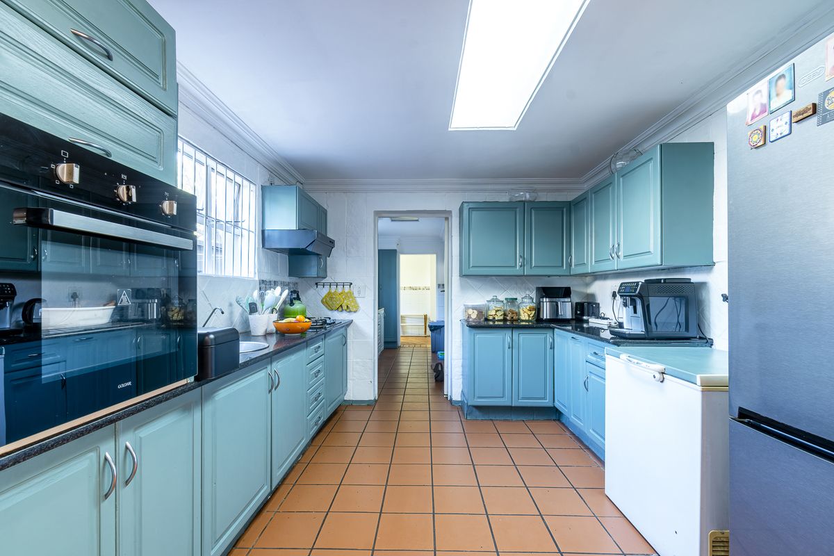 A functional kitchen featuring teal cabinetry, built-in oven, hob, and tiled flooring, offering a practical layout with ample storage space.