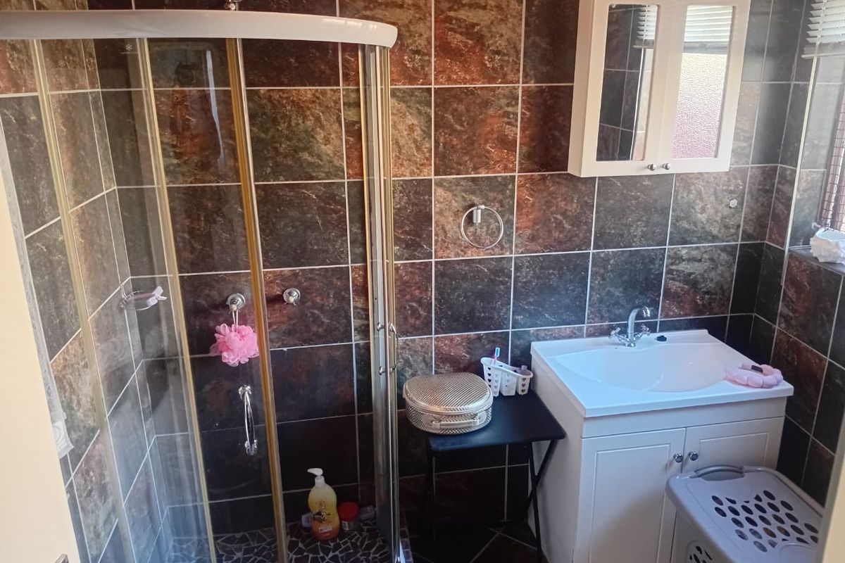 A functional bathroom featuring a corner shower enclosure, a white vanity unit with basin, and dark decorative wall tiling.