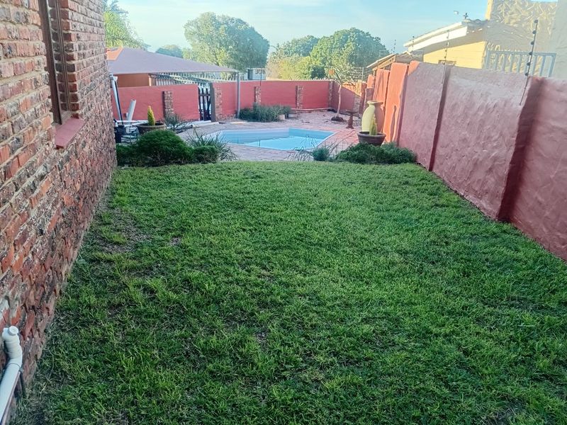 A private rear garden featuring a swimming pool, paved surround, and enclosed by brick boundary walls with electric fencing.