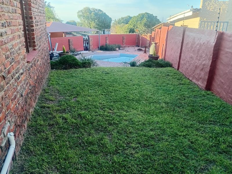 A private rear garden featuring a small swimming pool, paved surround, and established lawn, enclosed by high brick boundary walls with electric fencing.
