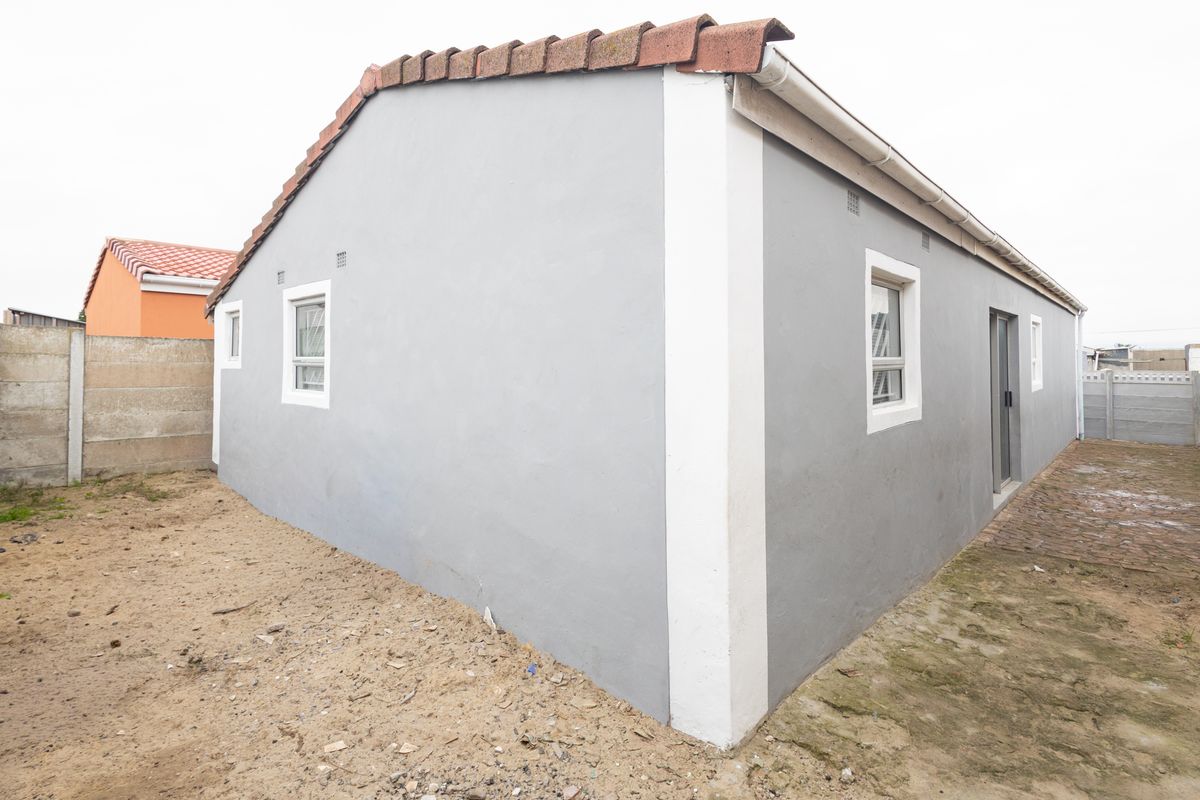 Rear exterior view of the property featuring grey painted walls, terracotta roof tiles, and a sliding door access point with surrounding unlandscaped ground.