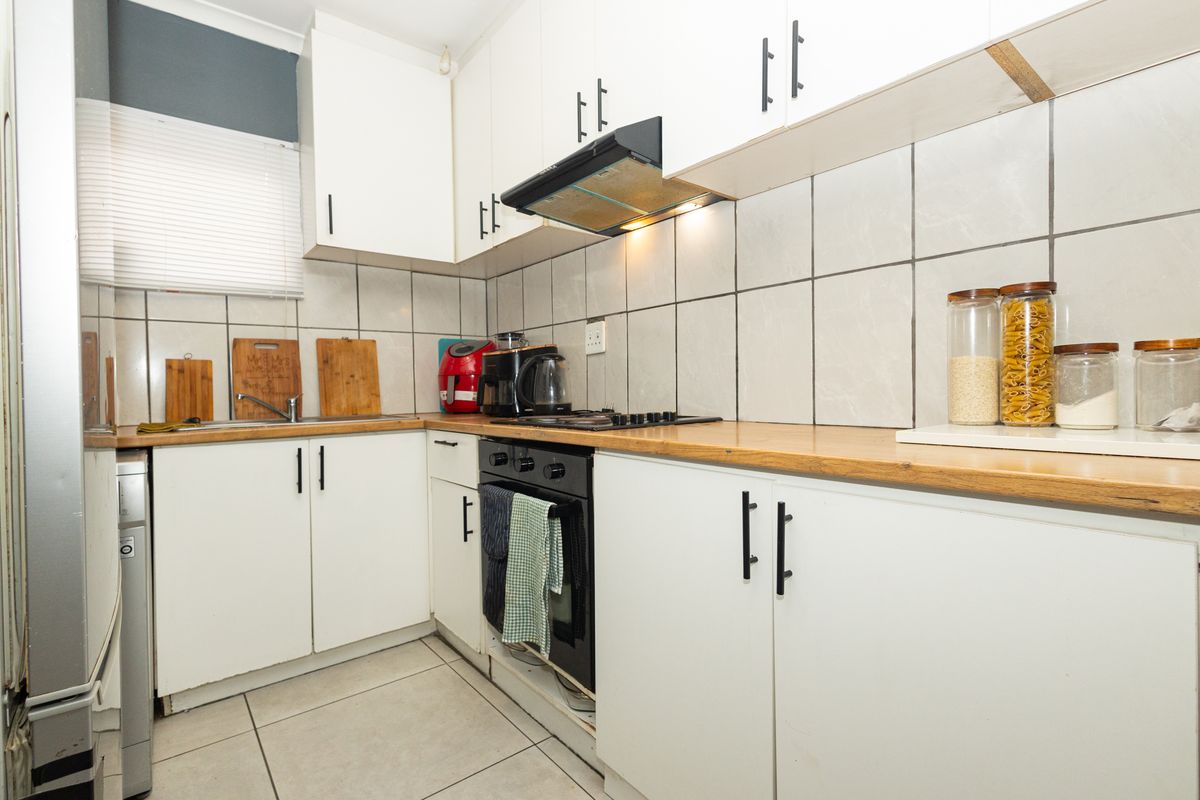 A functional kitchen featuring white cabinetry, wood-look laminate countertops, tiled splashbacks, and integrated cooking appliances.