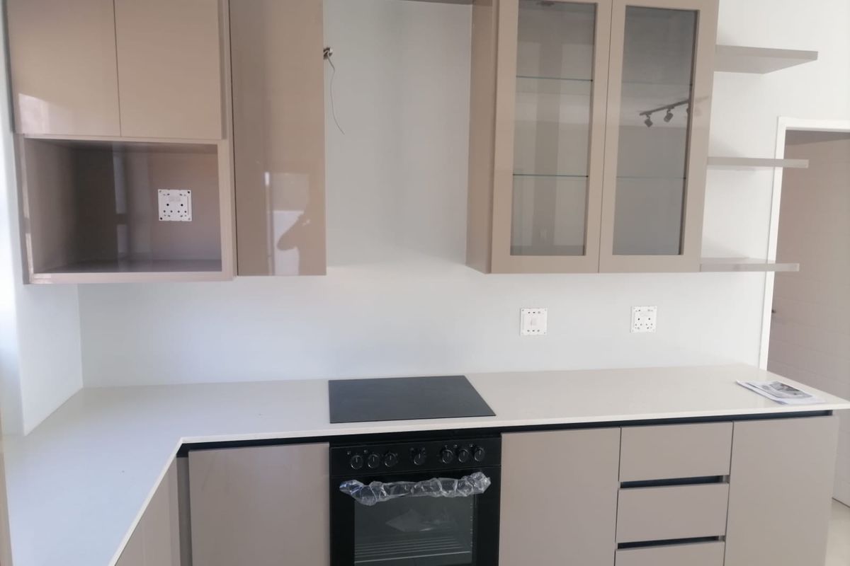 Modern kitchen featuring sleek taupe cabinetry, stone countertops, a built-in oven, and a glass-top hob, presenting a clean and contemporary aesthetic.