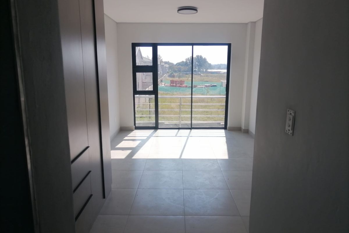 A bright, modern bedroom featuring neutral floor tiles, built-in cabinetry, and a large sliding glass door leading to a balcony with exterior views.