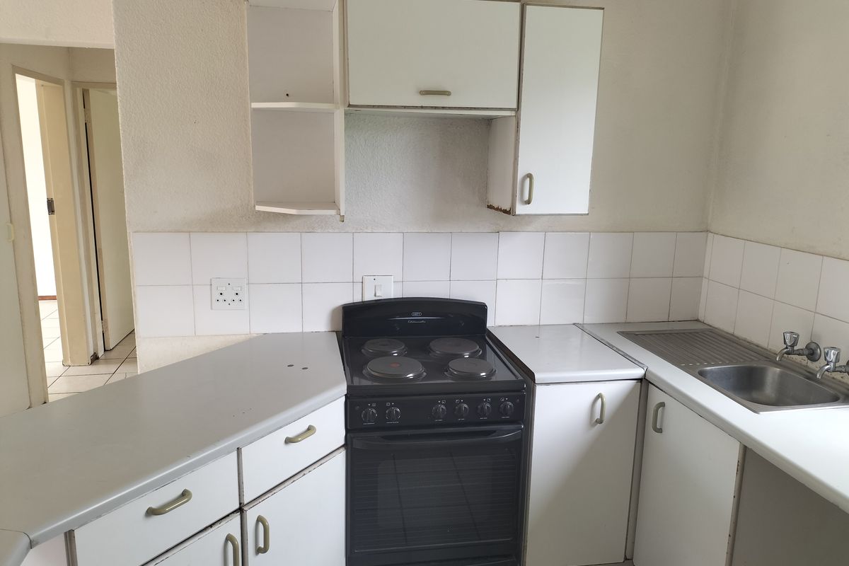 A compact, dated kitchen featuring white cabinetry, a tiled backsplash, and a freestanding electric stove, offering potential for a modern renovation.