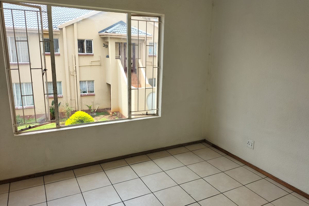 An empty bedroom featuring tiled flooring, security bars on the window, and a view of the adjacent apartment building.