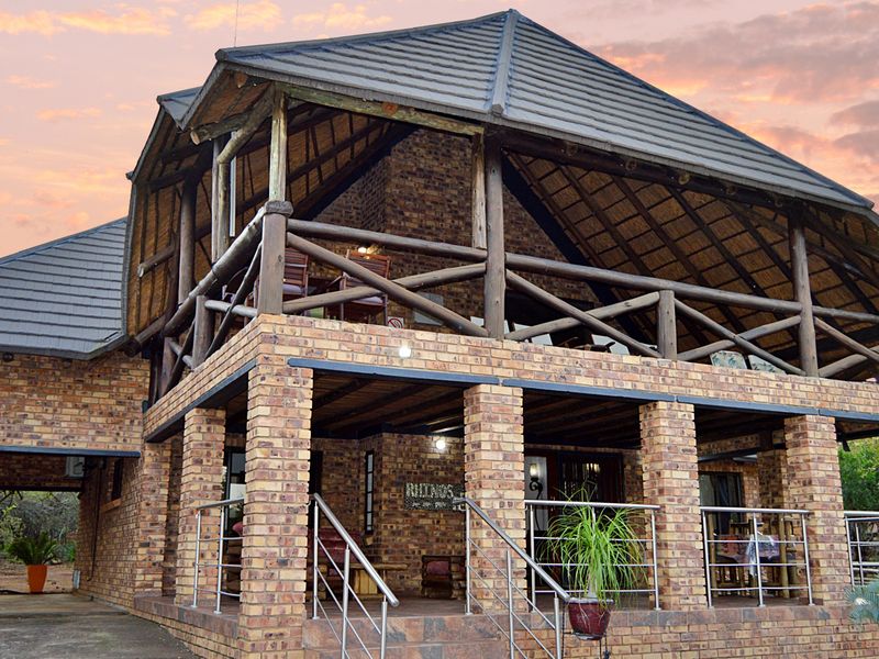 A charming double-story house featuring exposed brickwork, a traditional thatched roof, and a spacious covered patio with a timber balcony above.