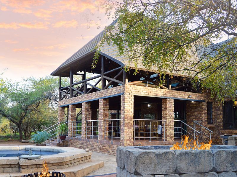 A charming bushveld-style home featuring an exposed brick facade, a spacious covered patio with timber beams, a stone-clad swimming pool, and a built-in fire pit.