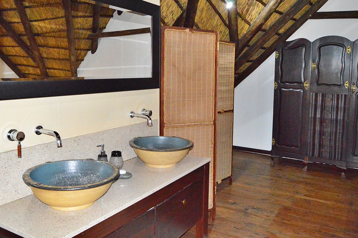 A unique bathroom featuring a double vanity with stone countertop, vessel sinks, and exposed thatch roof with timber trusses.