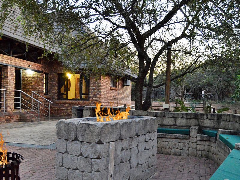 Outdoor patio area featuring a brick facade, paved flooring, stainless steel railing, and a built-in stone fire pit with integrated seating.
