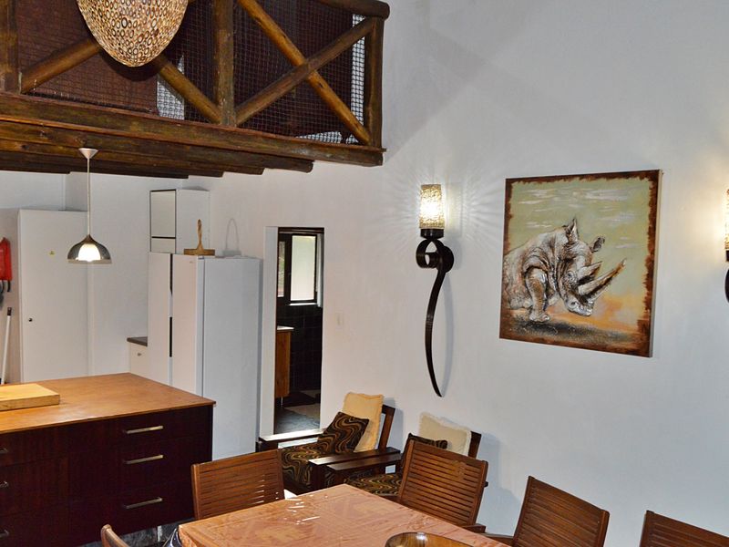 Open plan living and dining area featuring a timber mezzanine loft, kitchen island, and decorative wall sconces.