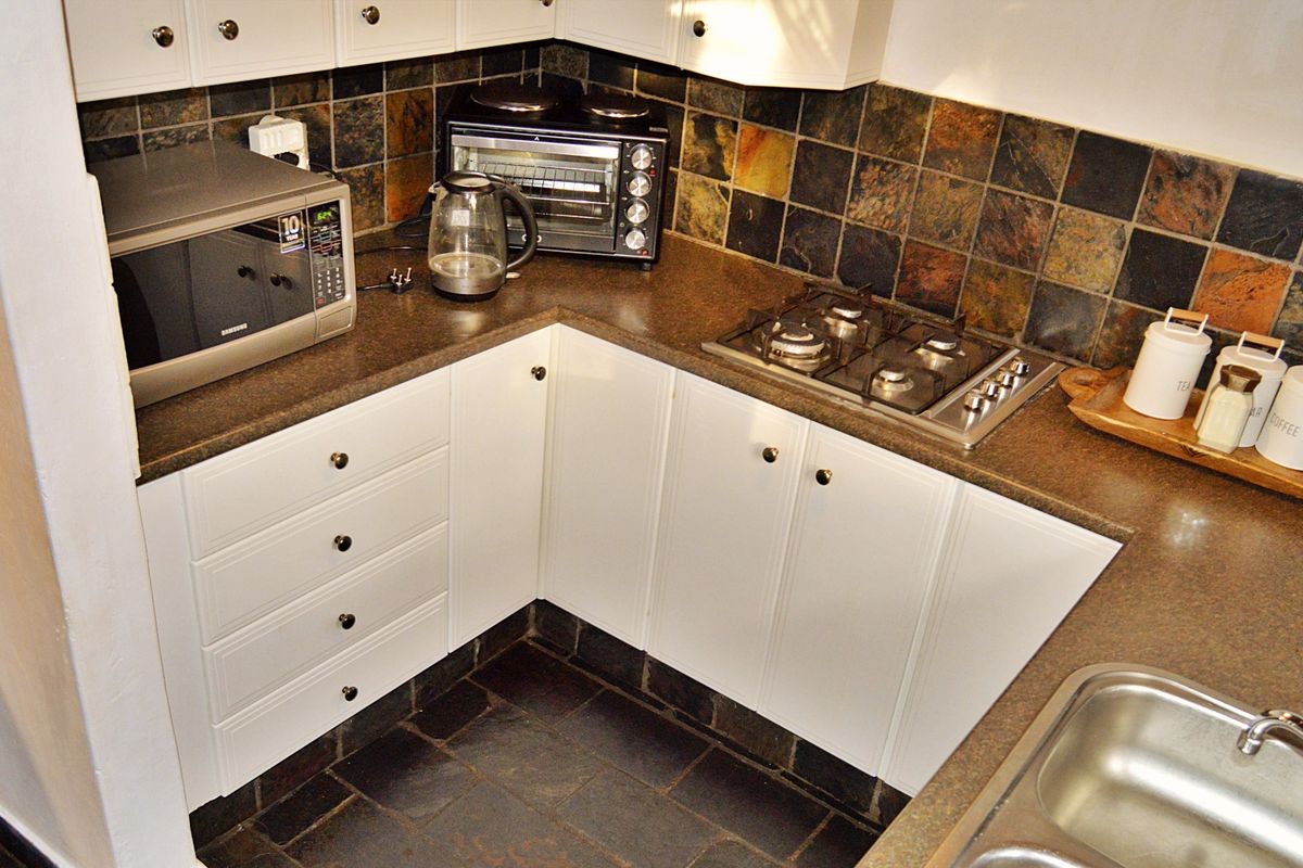 Compact kitchen featuring white cabinetry, dark laminate countertops, a gas hob, and slate tile finishes on both the backsplash and flooring.