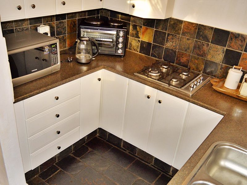 Compact kitchen featuring white cabinetry, dark laminate countertops, a gas hob, and slate tile finishes on both the backsplash and flooring.