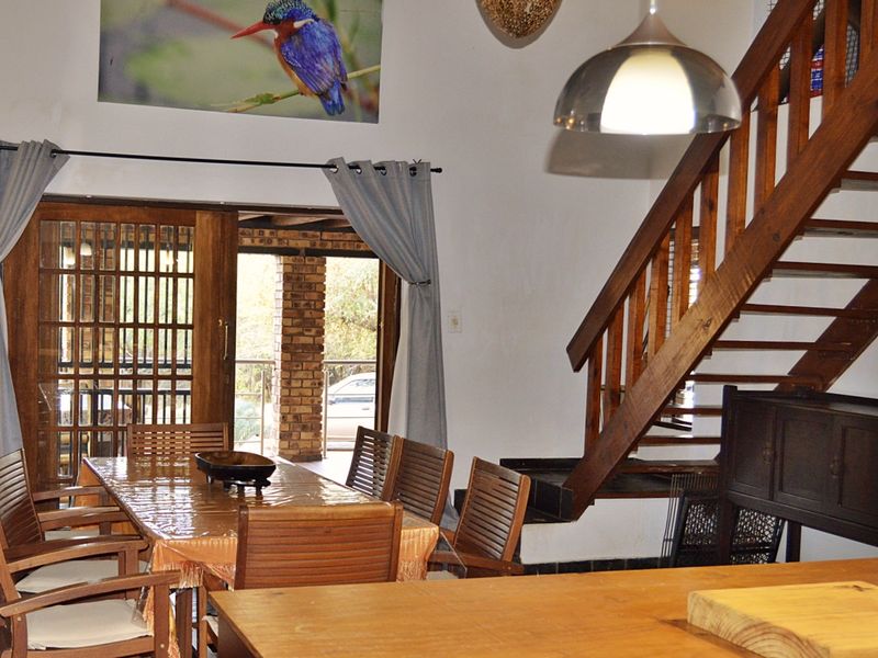 Open plan living and dining area featuring a wooden staircase, pendant lighting, and sliding glass doors leading to an outdoor patio space.