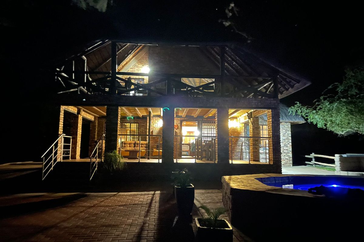 Night view of a double-story brick house featuring a thatched roof, covered patio, balcony, and a swimming pool in the foreground.