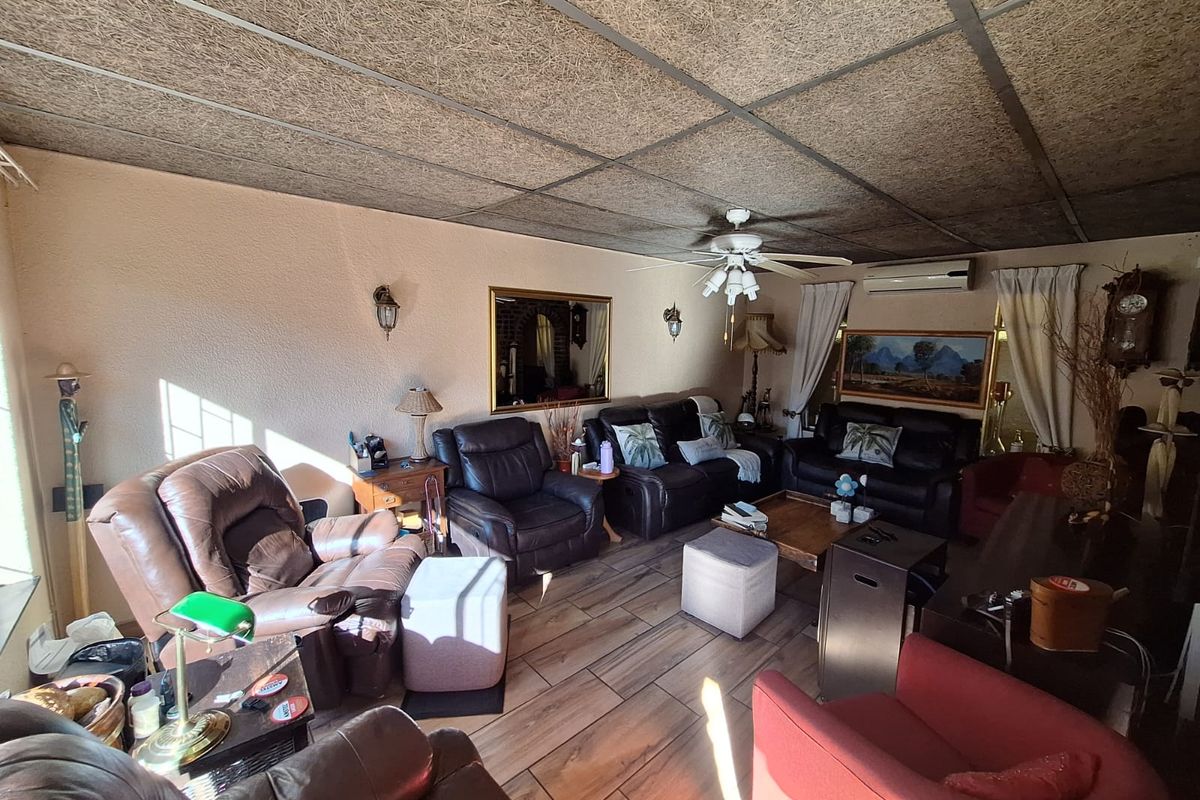 Spacious living room featuring wood-look tile flooring, a ceiling fan, and a wall-mounted air conditioning unit for climate control.