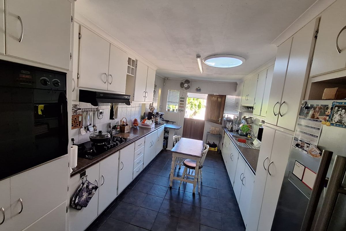 A functional galley-style kitchen featuring white cabinetry, dark laminate countertops, built-in oven, gas hob, and tiled flooring with natural light from a skylight.