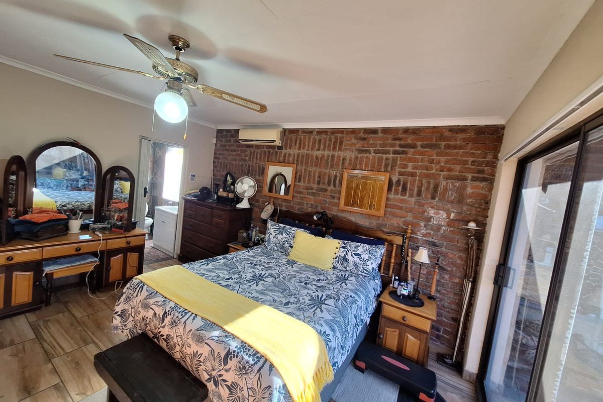 Spacious bedroom featuring an exposed brick wall, ceiling fan, split-system air conditioning, and direct access to the outdoors via sliding glass doors.