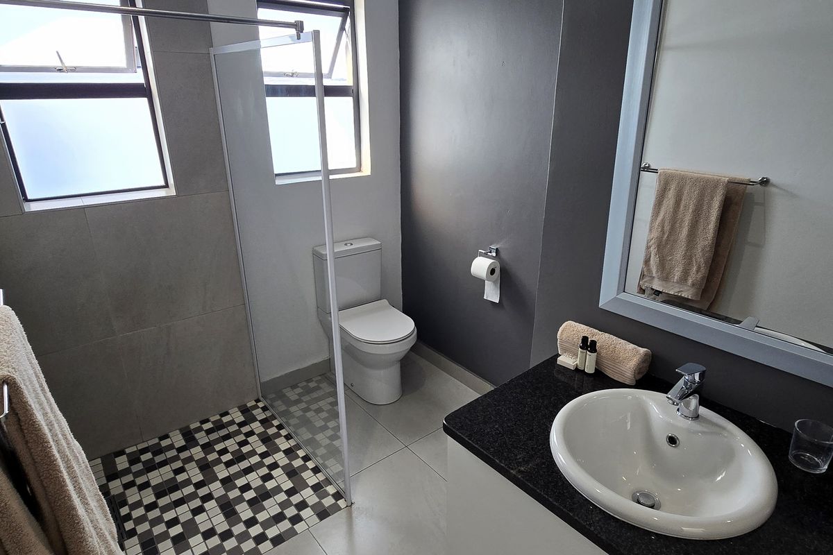 Modern bathroom featuring a walk-in shower with glass screen, granite-topped vanity, and contemporary tiled finishes.