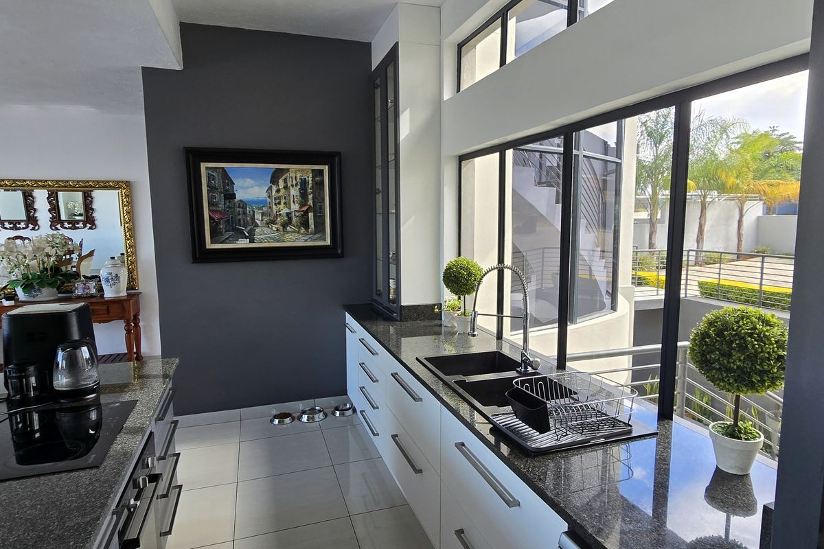 Modern kitchen featuring sleek white cabinetry, dark granite countertops, an induction hob, and large windows providing ample natural light and garden views.