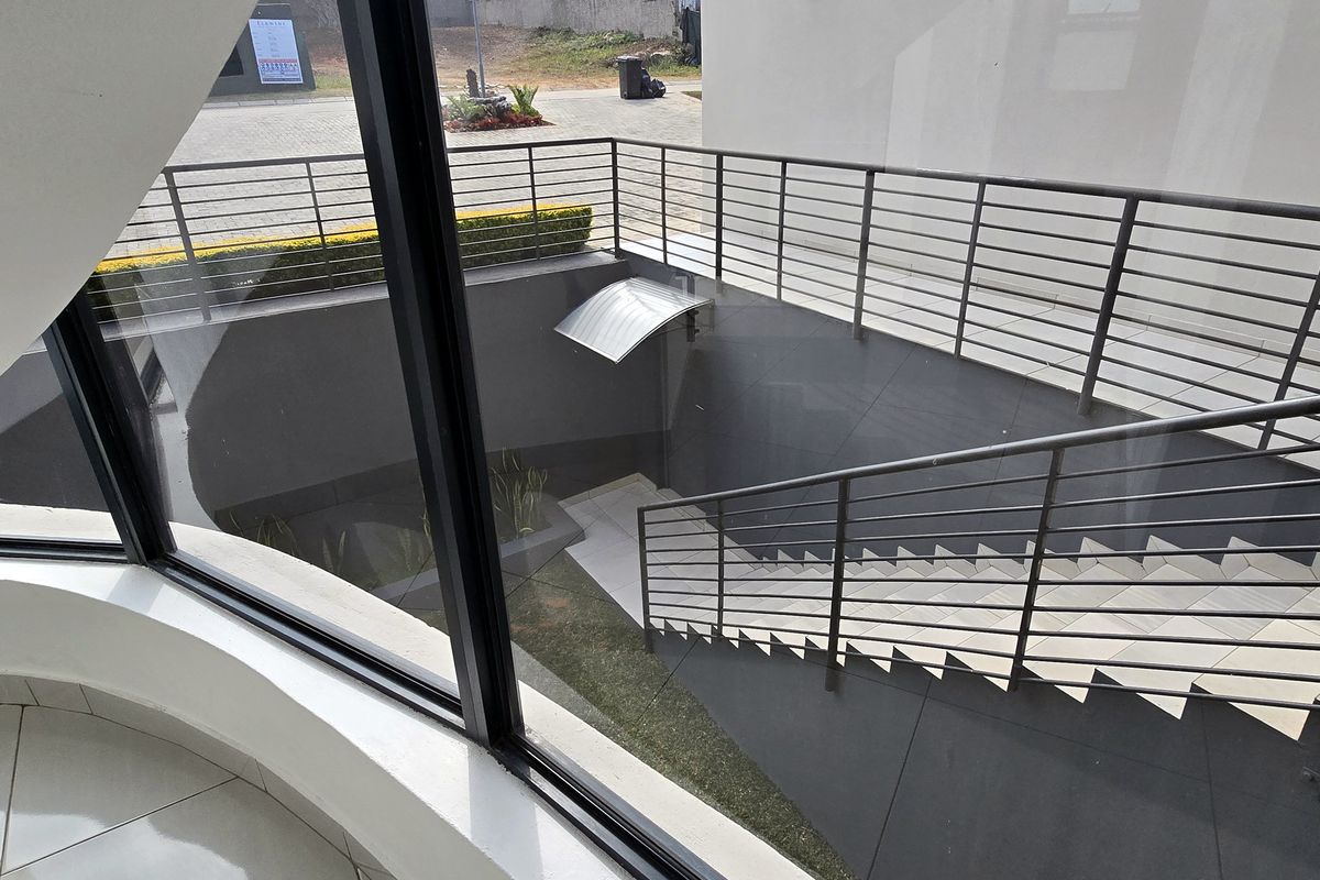 A modern exterior view featuring a tiled staircase with metal railings leading down to a lower level, viewed through a large glass window.
