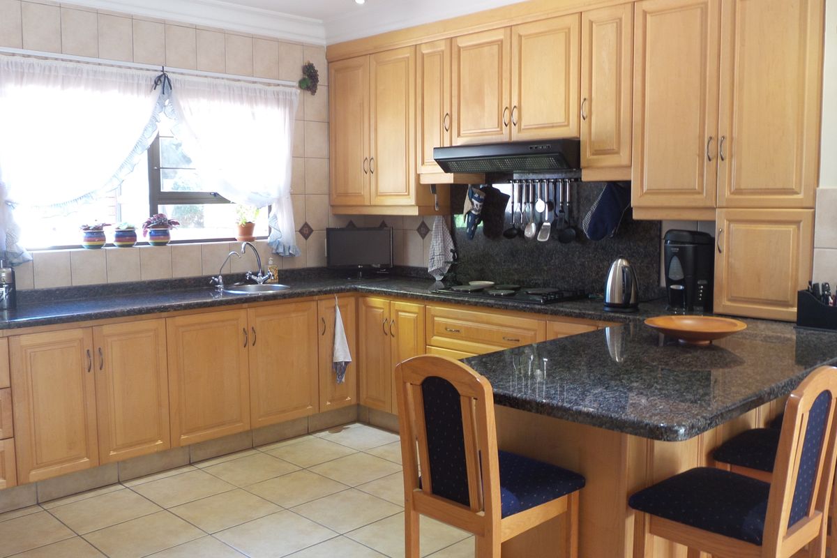 A functional kitchen featuring wooden cabinetry, granite countertops, a built-in hob with extractor fan, and tiled flooring.
