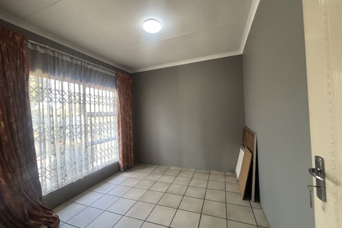 A vacant bedroom featuring neutral grey walls, tiled flooring, and a large window fitted with a security gate.