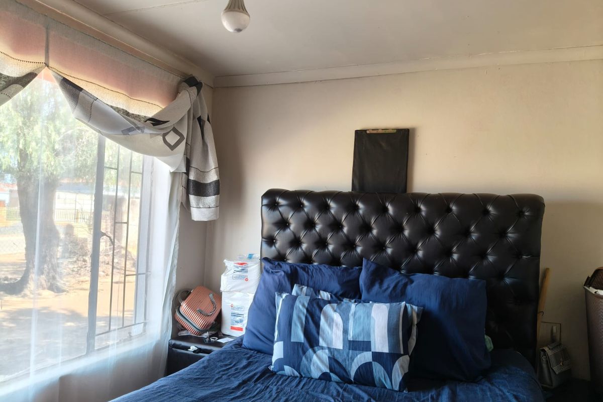 A bedroom featuring a window with security bars and visible signs of wear on the ceiling and walls.