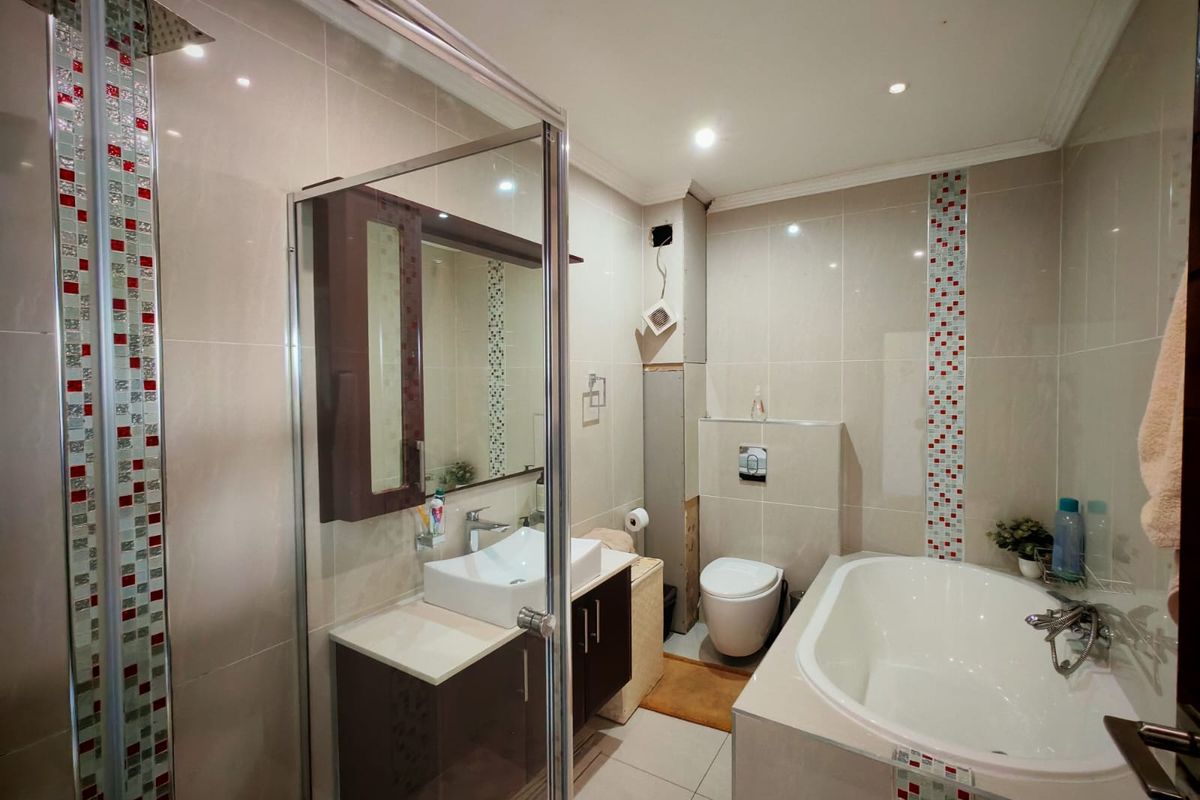 Modern bathroom featuring a glass-enclosed shower, built-in bathtub, wall-mounted toilet, and vanity with vessel sink, accented by decorative mosaic tiling.