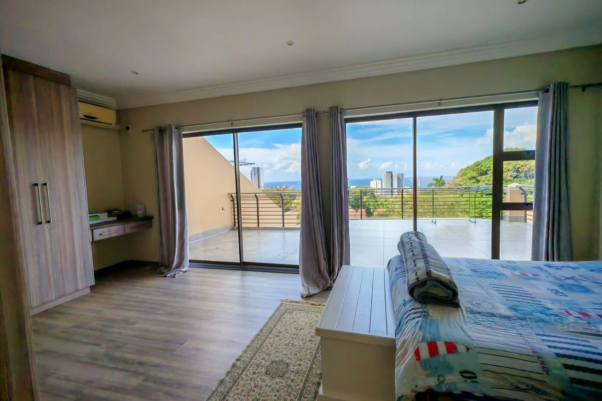 Spacious bedroom featuring laminate flooring, built-in wardrobes, and large sliding glass doors opening onto a private balcony with scenic coastal and city views.