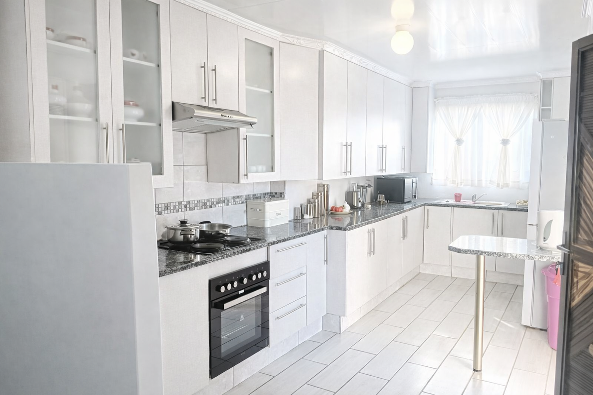 A bright, well-maintained kitchen featuring white cabinetry, granite countertops, built-in oven, hob, extractor fan, and tiled flooring.
