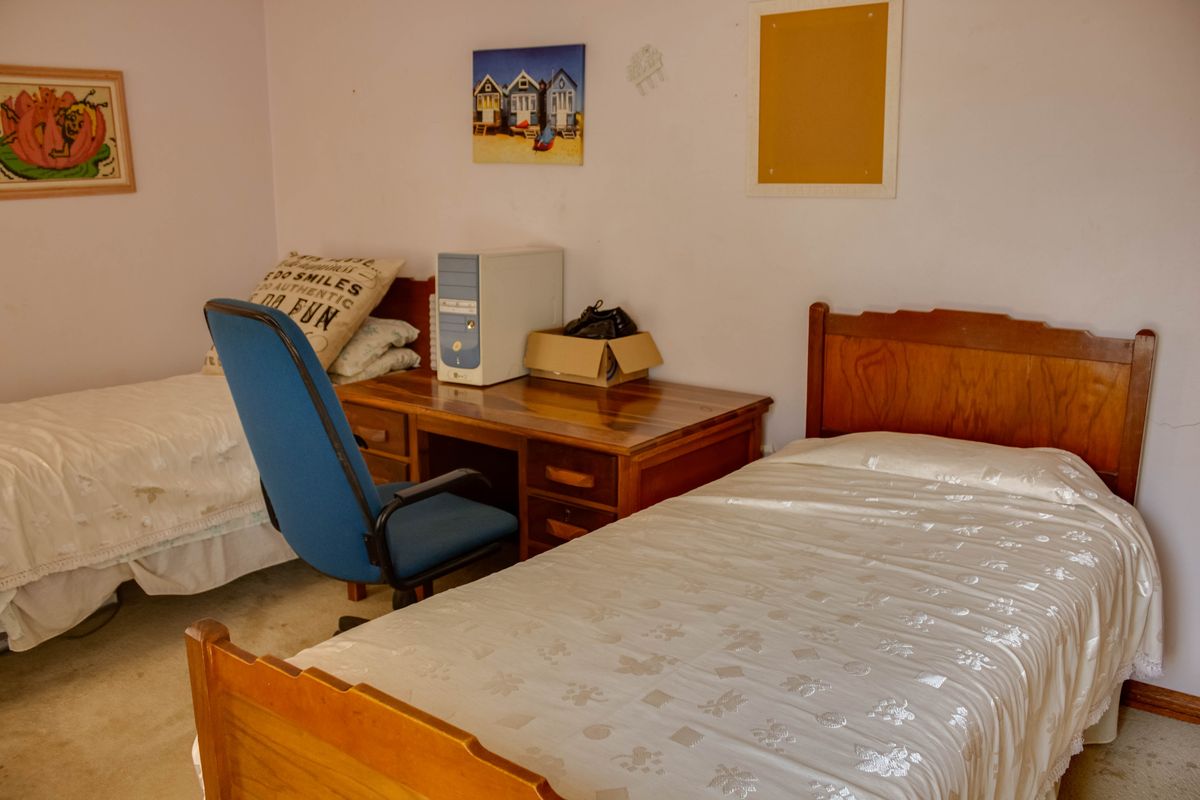 A bedroom featuring carpeted flooring and plain walls, currently furnished with two single beds and a wooden desk.