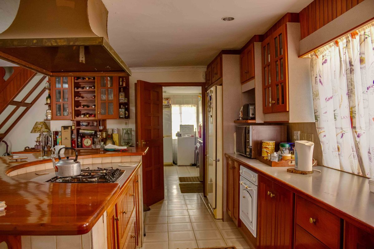 A functional kitchen featuring timber cabinetry, gas hob with extractor, and tiled flooring, offering a traditional layout with potential for modern updates.