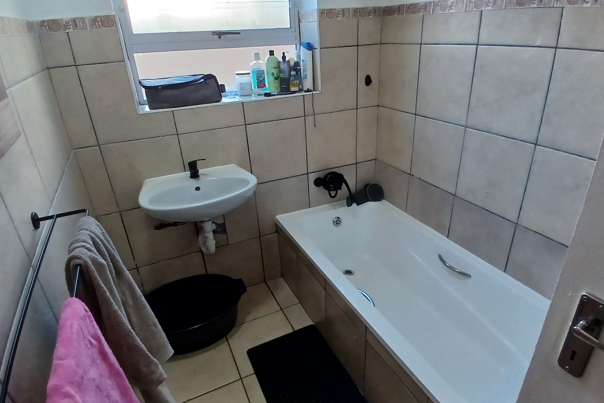 A compact bathroom featuring a standard bathtub, wall-mounted basin, and tiled walls and flooring.