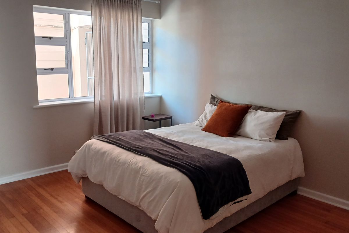 A well-lit bedroom featuring warm-toned laminate flooring and a large window that provides natural light.