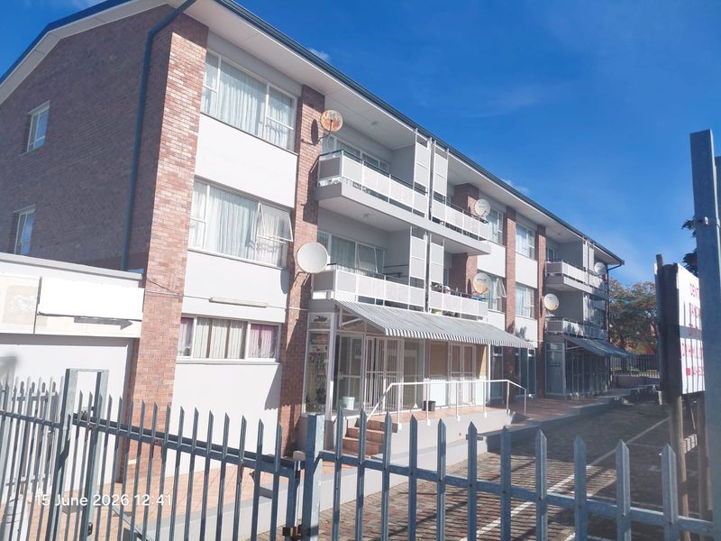 Exterior view of a multi-story apartment building featuring brick and plaster facade, private balconies, and secure perimeter fencing.
