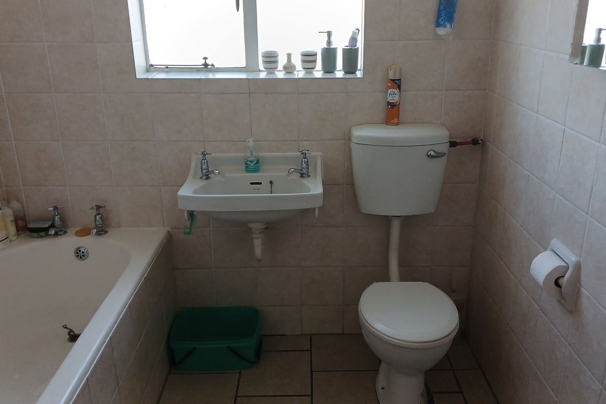 A functional bathroom featuring a standard bathtub, wall-mounted basin, and a close-coupled toilet with neutral wall tiling throughout.