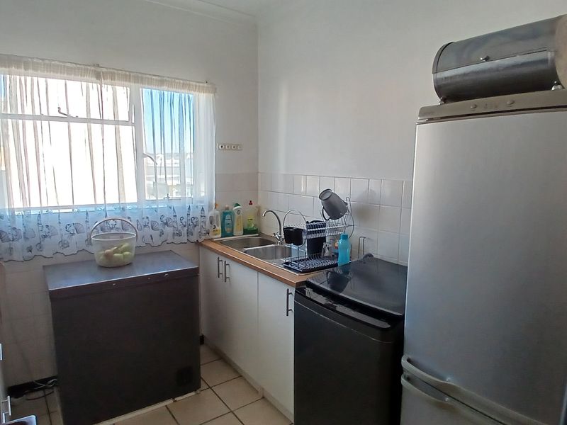 A functional kitchen featuring white cabinetry, tiled splashbacks, a stainless steel sink, and tiled flooring, offering a practical layout for daily meal preparation.