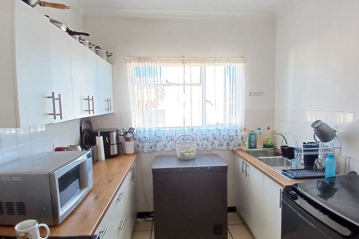 A functional kitchen featuring white cabinetry, wood-look countertops, tiled splashbacks, and a stainless steel sink, offering a practical layout for daily meal preparation.