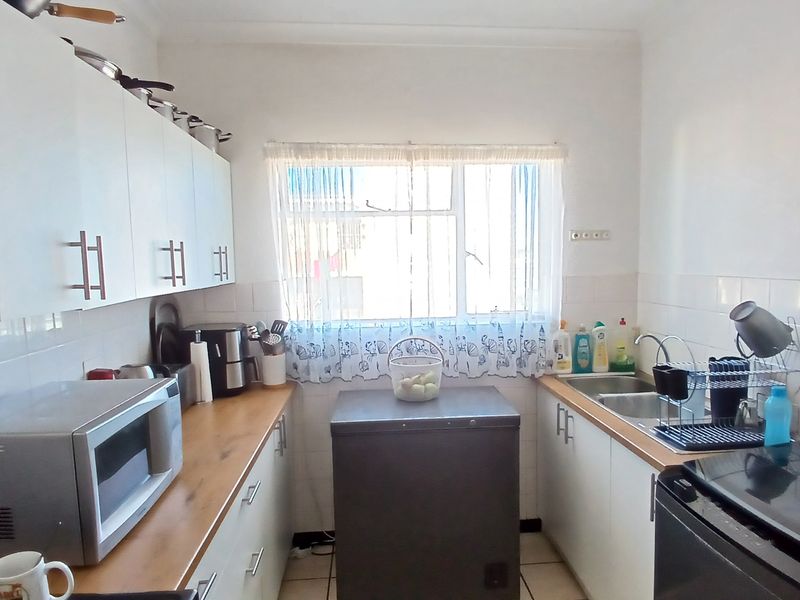 A functional kitchen featuring white cabinetry, wood-look countertops, tiled splashbacks, and a stainless steel sink, offering a practical layout for daily meal preparation.