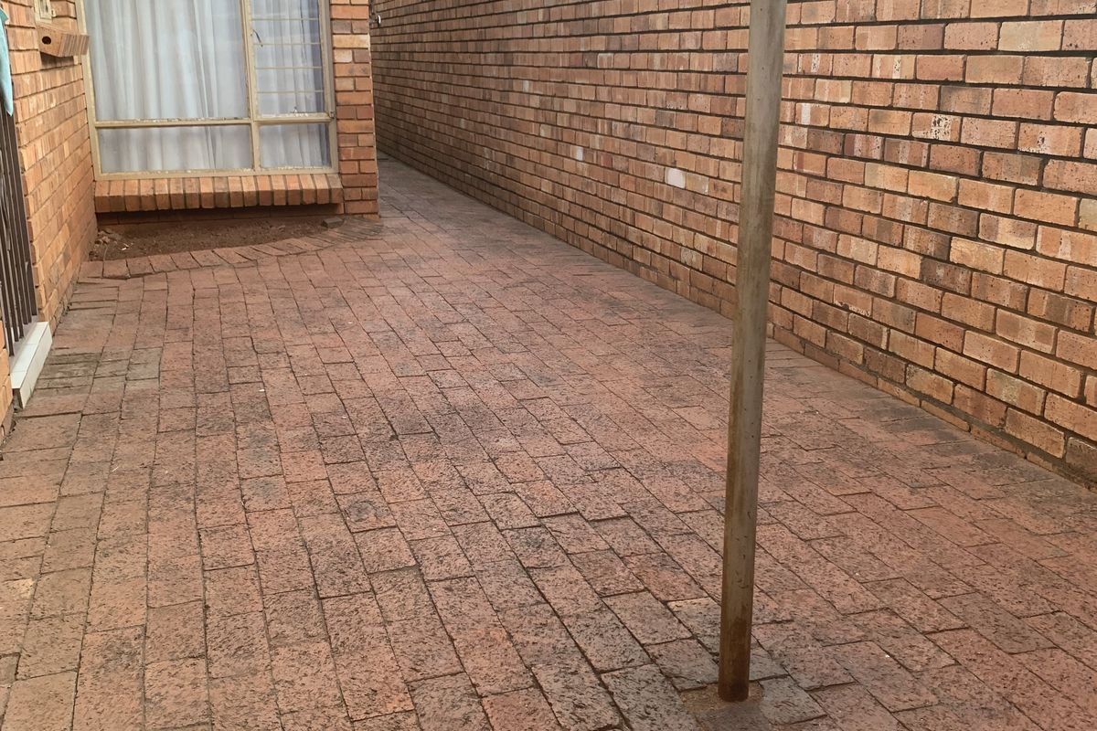 A paved rear courtyard area featuring a brick boundary wall and a central metal washing line pole.